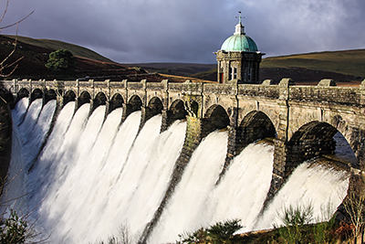 Elan Valley Dam in full flood-flow.&nbsp; Early winter morning with low sun on dam and grey stormy clouds overhead.